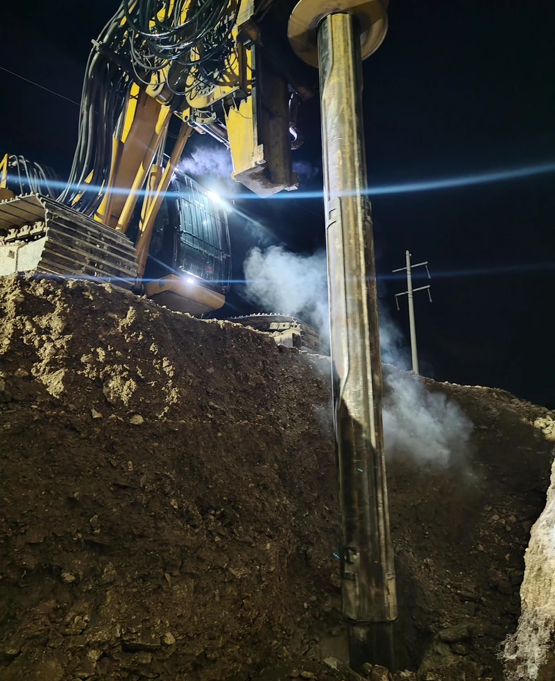 Perforadora trabajando de noche dentro de la excavación, con el ademe descendiendo al barreno